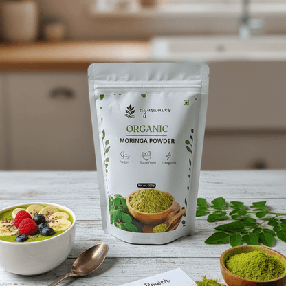 Ayurwaves Organic Moringa Powder package on a kitchen counter with a bowl of greens and leaves.